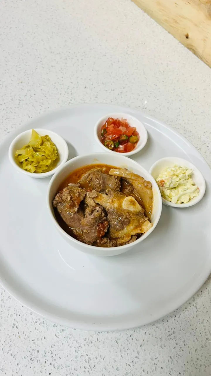 Tripe and beef stew served with cabbage, salsa and coleslaw sides